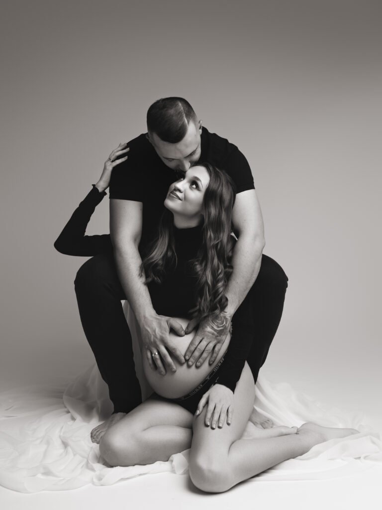 Para przytulająca się do brzucha na tle czarnej kurtyny